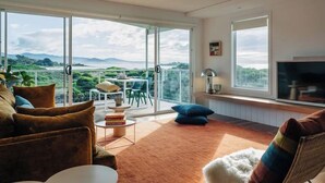 A spacious living room with a large sliding glass door leading to a balcony with a scenic view. - Frankie Beach House Bicheno (Glamorgan-Spring Bay)