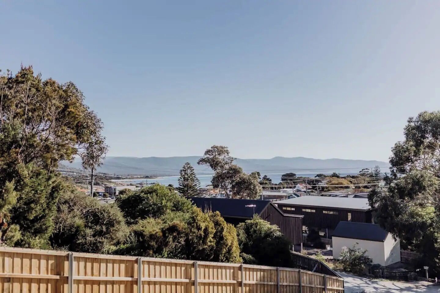 A coastal view with a wooden fence, buildings, and trees.