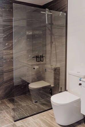 Une salle de bain moderne avec une douche à parois de verre, des toilettes blanches et un sol carrelé en marbre.