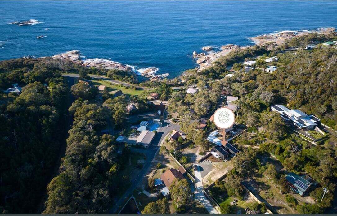 An aerial view of a coastal property with a central building surrounded by dense vegetation and rocky outcrops.