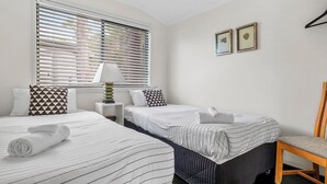 A hotel room with two beds, a chair, a nightstand, and a window with blinds.