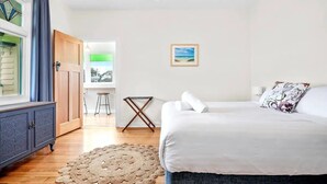 Una camera da letto con un letto, un armadietto in legno, un tappeto intrecciato, un quadro incorniciato e vista su un balcone.