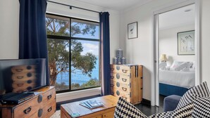 A room with a large window, a bed, a TV, a wooden chest, and a sofa.
