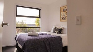 A bedroom with a bed, a window, and a painting on the wall.