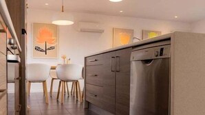 A modern kitchen with a dishwasher, a dining area with chairs, and pendant lighting.