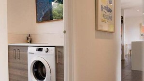 A laundry area with a washing machine, a wooden cabinet, and a framed poster on the wall.