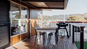 Una terraza al aire libre con una mesa y sillas de madera, una parrilla y vistas del paisaje circundante.