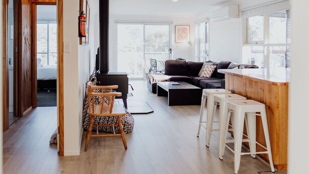 Una sala moderna con sofá, mesa de centro y taburetes de bar. Se observa una chimenea al fondo.
