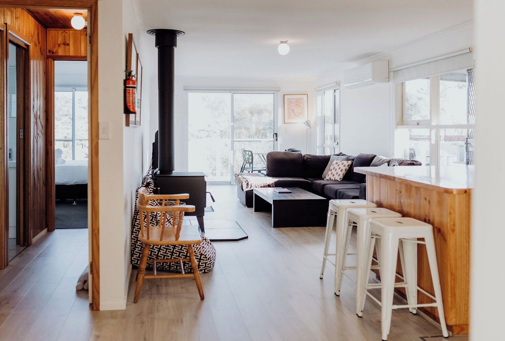 Un salon moderne avec un canapé, une table basse et des tabourets de bar. On aperçoit une cheminée au fond.