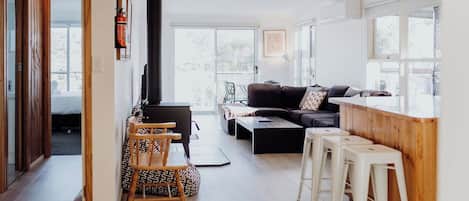 Een moderne woonkamer met een bank, salontafel en barstoelen. Achtergrond is een open haard zichtbaar.