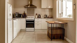 Una cocina moderna con gabinetes blancos, una campana extractora de acero inoxidable, un microondas, un horno y una pequeña mesa con una cesta.