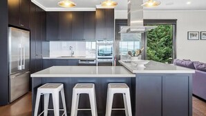 Una cocina moderna con armarios oscuros, una isla grande con taburetes, electrodomésticos de acero inoxidable e iluminación colgante.