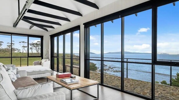Un salón moderno con ventanas amplias, una pared de piedra y vista al mar.