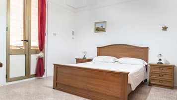 A bedroom with a wooden bed, two bedside tables, a nightstand, a red curtain, a window, and a small picture on the wall.