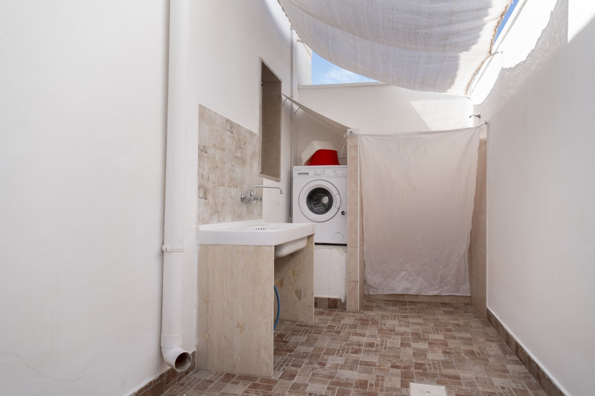 A compact laundry room with a washing machine, a sink, and a tiled floor.