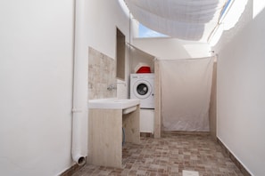 Uma lavanderia compacta com máquina de lavar, pia e chão revestido com azulejos.