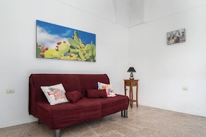 Una habitación con un sofá rojo, una pintura de un cactus, una mesita con una lámpara y un cuadro en la pared.