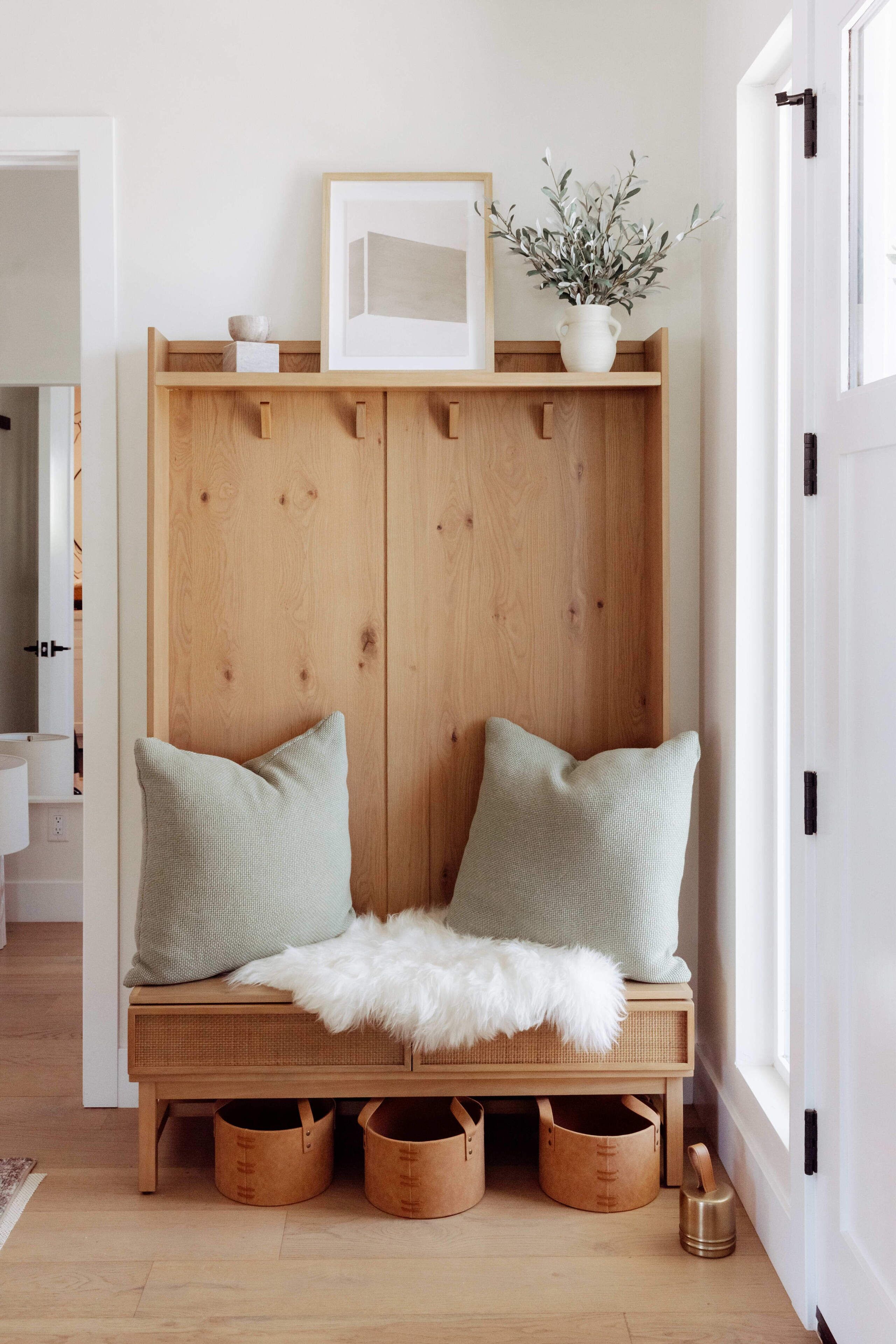 A wooden bench with two pillows, a white furry throw, and a framed picture above it.
