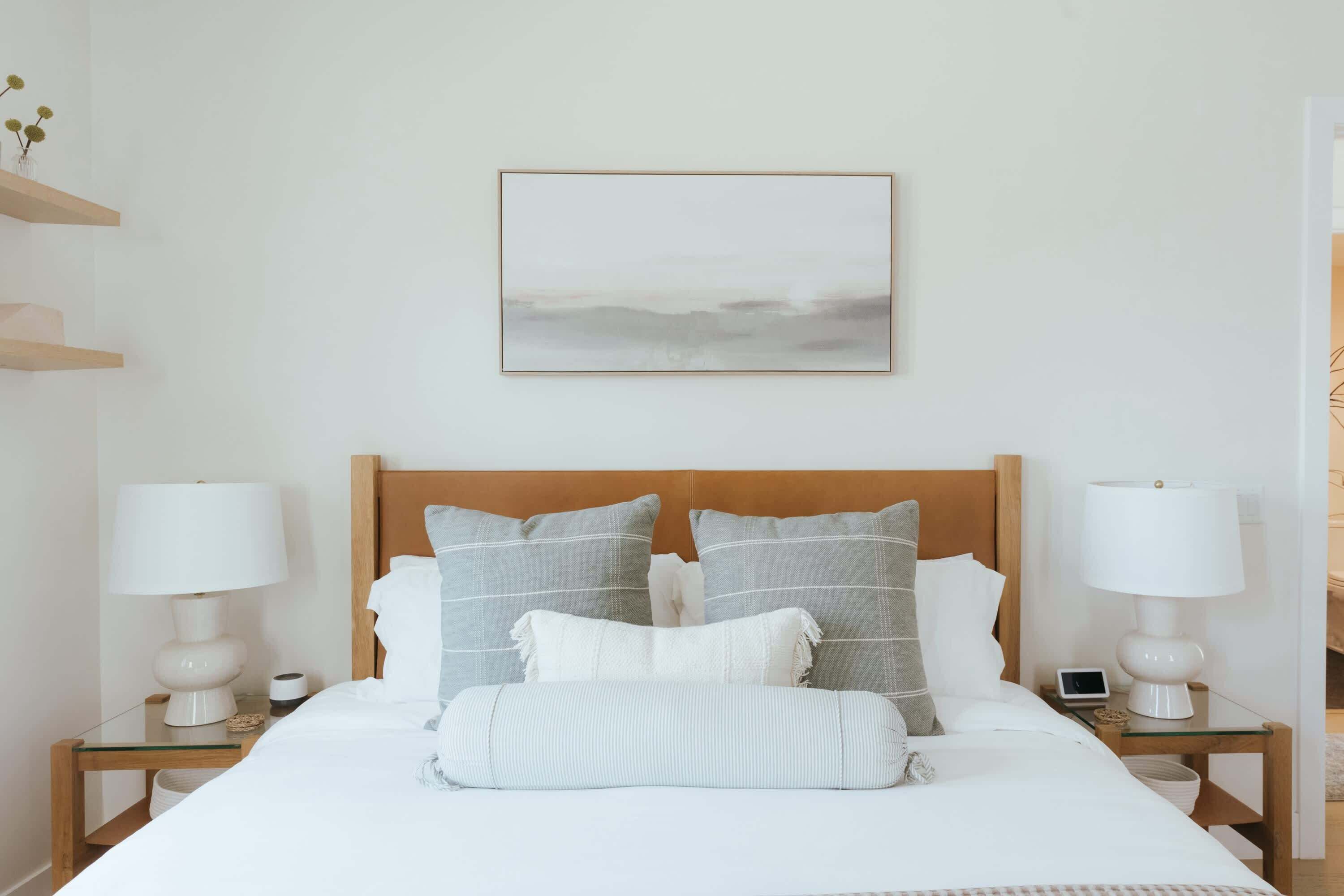 Un dormitorio ordenado con cabecera de madera, dos mesitas de noche con lámparas, una cama con ropa de cama blanca y un cuadro enmarcado en la pared.