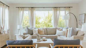 Een moderne woonkamer met een beige bank, twee fauteuils, een salontafel en een lamp.
