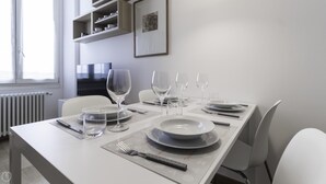 A dining table set with plates, glasses, and cutlery in a modern, minimalistic room with white walls and a radiator. - Italianway Easy - Sarpi 10 B (Milan)