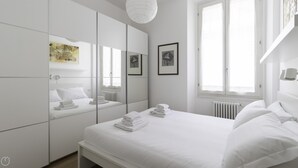 A modern, white-themed bedroom with a large bed, a built-in wardrobe, and a large mirror. - Italianway Easy - Sarpi 10 B (Milan)
