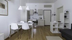 A modern kitchen with white cabinets, stainless steel appliances, and pendant lighting. There is a dining area with a white table and chairs. - Italianway Easy - Sarpi 10 B (Milan)