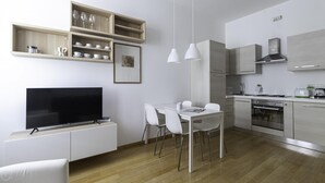 A modern kitchen with a dining area, built-in shelves, and a flat-screen TV. - Italianway Easy - Sarpi 10 B (Milan)