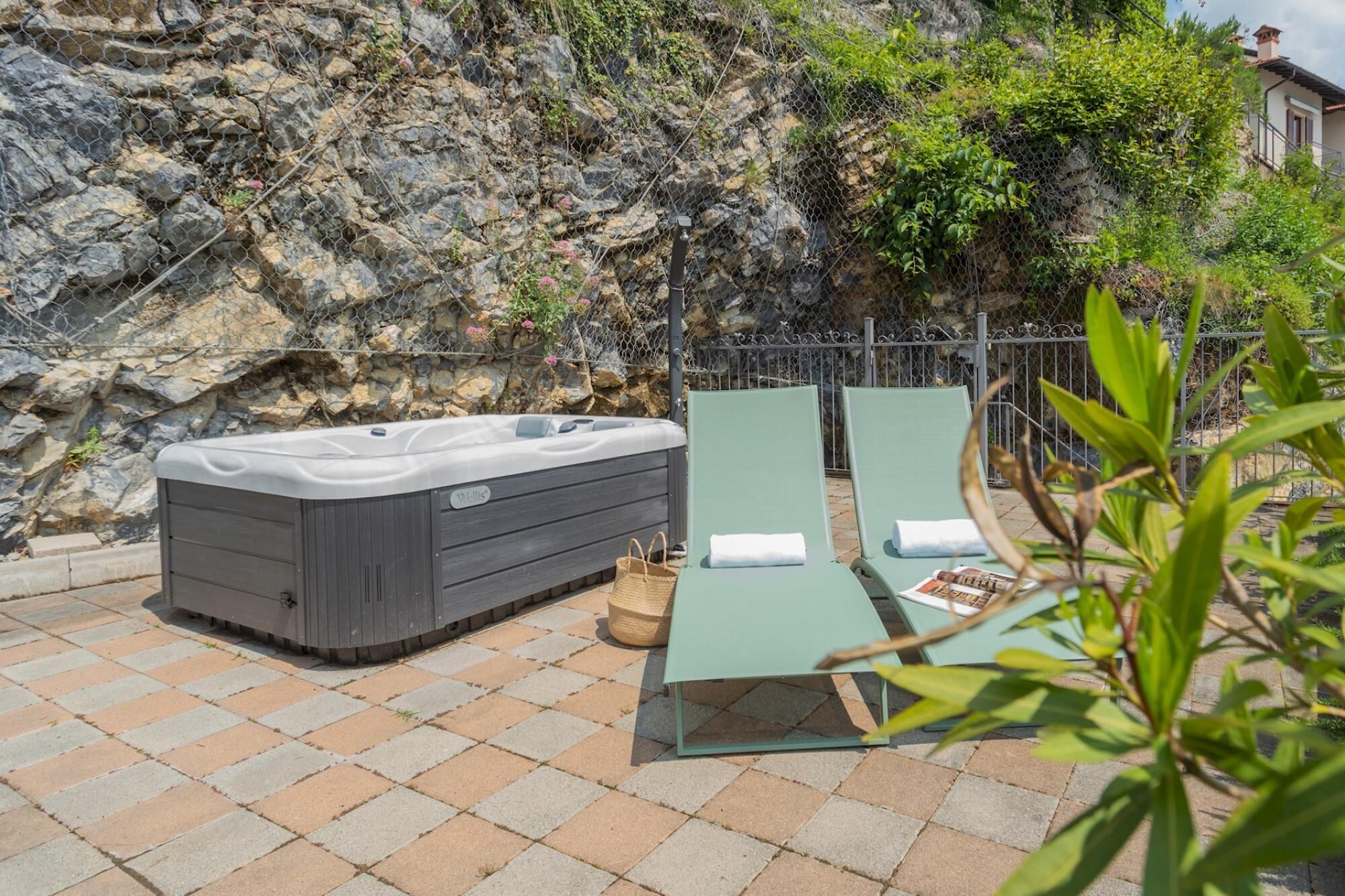 A hot tub and two lounge chairs on a stone patio with a rocky backdrop.