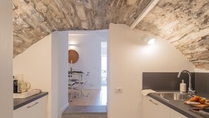 Une cuisine avec un plafond en pierre, un évier et un plan de travail sur lequel on voit des tomates.