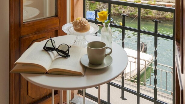 Un petit balcon avec une table, un livre, une paire de lunettes, une tasse et une fleur jaune.