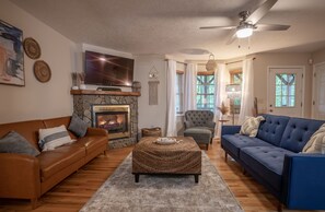 A living room with a stone fireplace, a television, a ceiling fan, and a blue sofa.