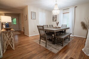 A dining area with a wooden table, chairs, a chandelier, and a rug.