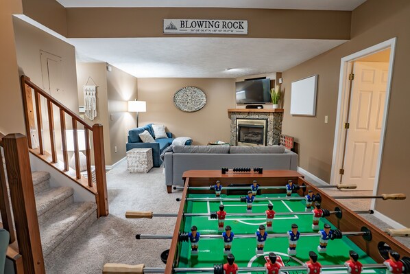 A living room with a foosball table, a sofa, a TV, and a fireplace.