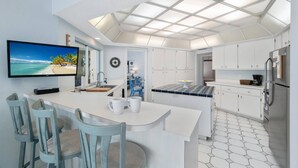 Een moderne keuken met een centraal eiland, witte kasten, een groot raam en een plafond met een geometrisch patroon.