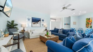 Een woonkamer met een witte bank, een blauwe bank en een eethoek met blauwe stoelen.