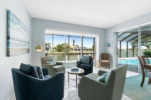 Amplia sala de estar con vistas a un lago y una piscina, con muebles modernos y grandes ventanales.