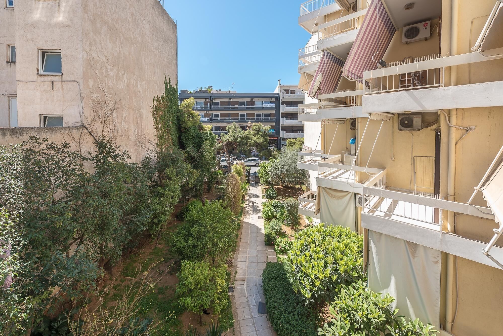 A narrow pathway between buildings with balconies, surrounded by greenery and trees.