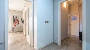 Un pasillo con pared azul claro, una puerta con un pequeño ventanal y una lámpara en la pared.