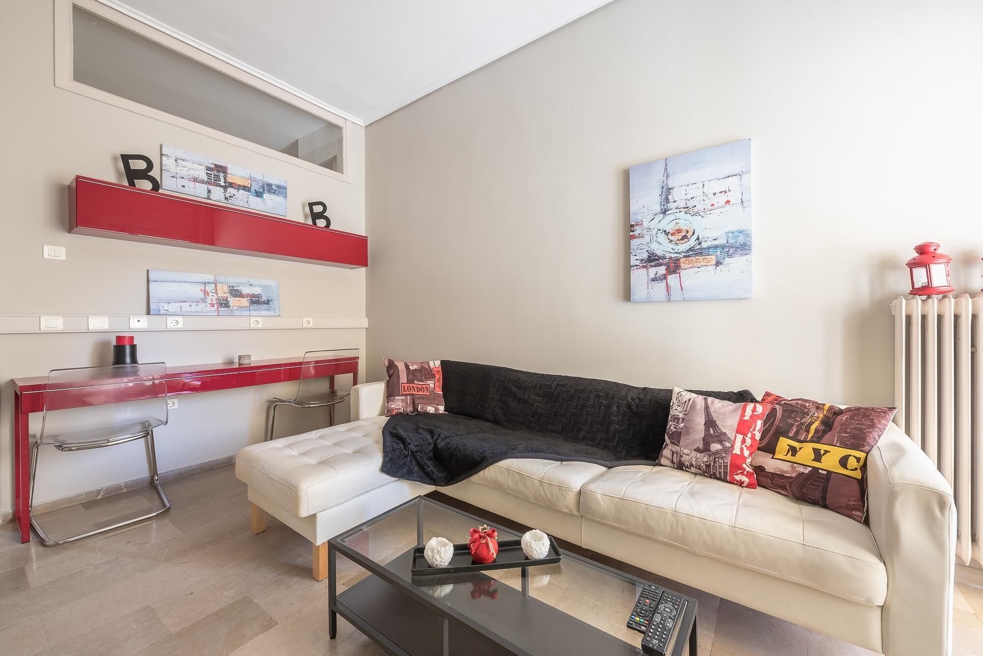 A living room with a sofa, a coffee table, a red desk, and a radiator.
