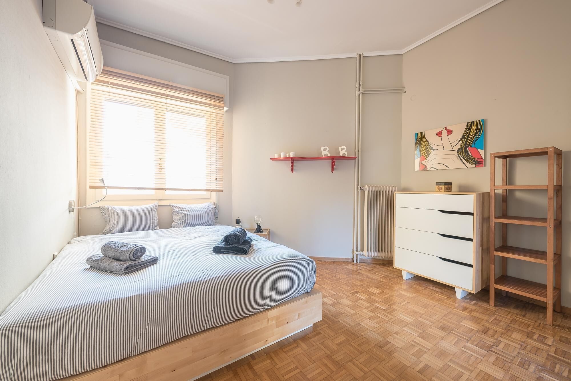 A bedroom with a bed, a radiator, a shelf with letters, and a painting on the wall.