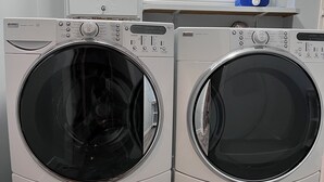 Two front-loading washing machines in a laundry room with a window and a blue water heater in the background. - Best garden private single room close LRT&free parking (Calgary)