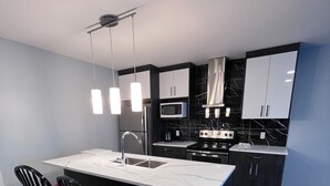 A modern kitchen with a central island, black chairs with red cushions, a microwave, and a stove. - Best garden private single room close LRT&free parking (Calgary)