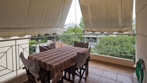 A balcony with a table and chairs, a view of the city, and a green hose on the wall. - Paradeisos in Chalandri (Marousi)