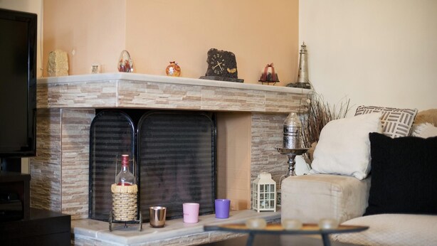 A living room with a stone fireplace, a television, and a sofa with a black cushion. - Paradeisos in Chalandri (Marousi)