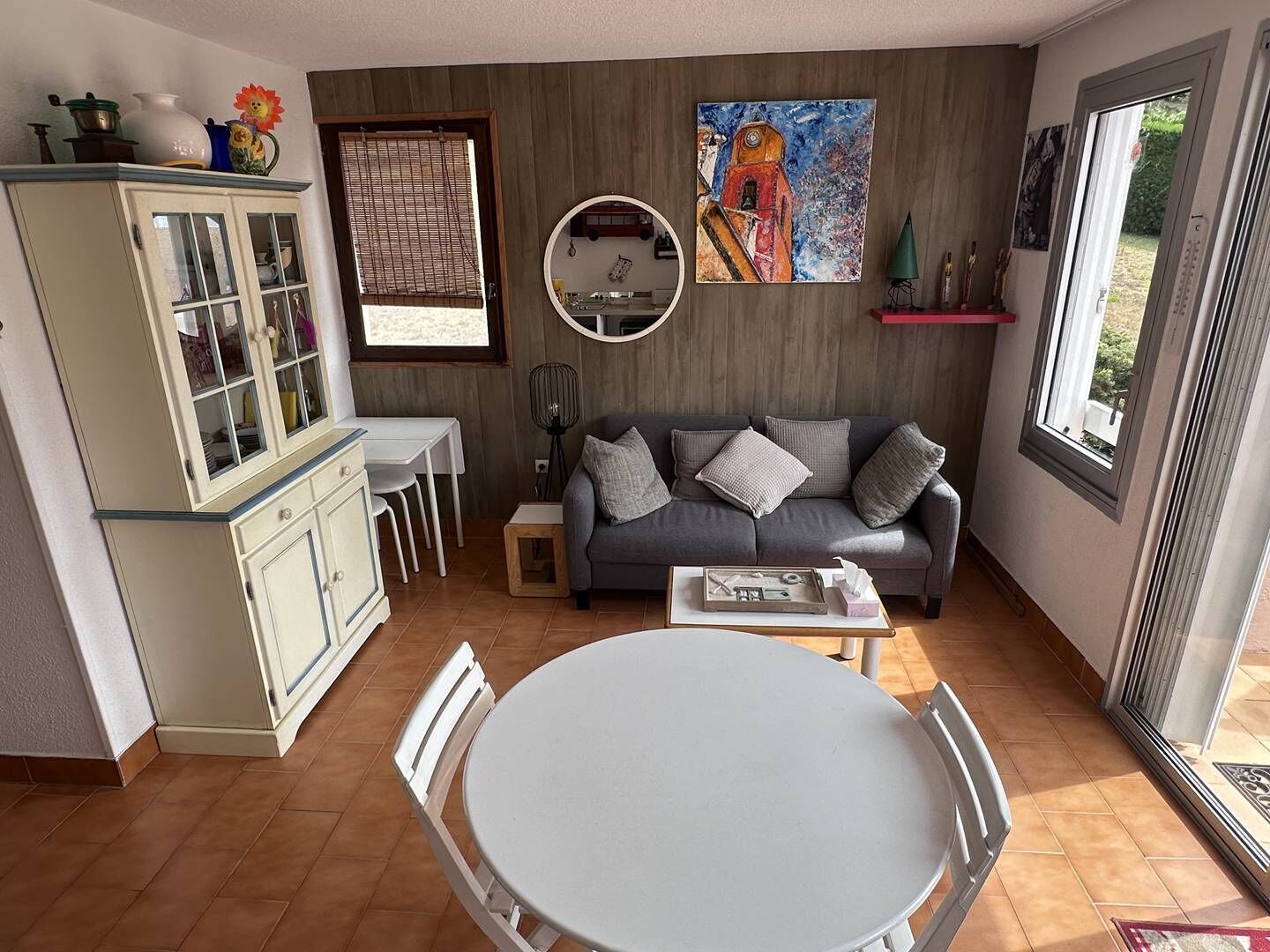 Ein gemütliches Wohnzimmer mit grauem Sofa, einem Esstisch und einer Vitrine.
