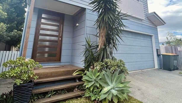 Et toetagers hus med en veranda, garage og en lille have med planter og et palmetræ.