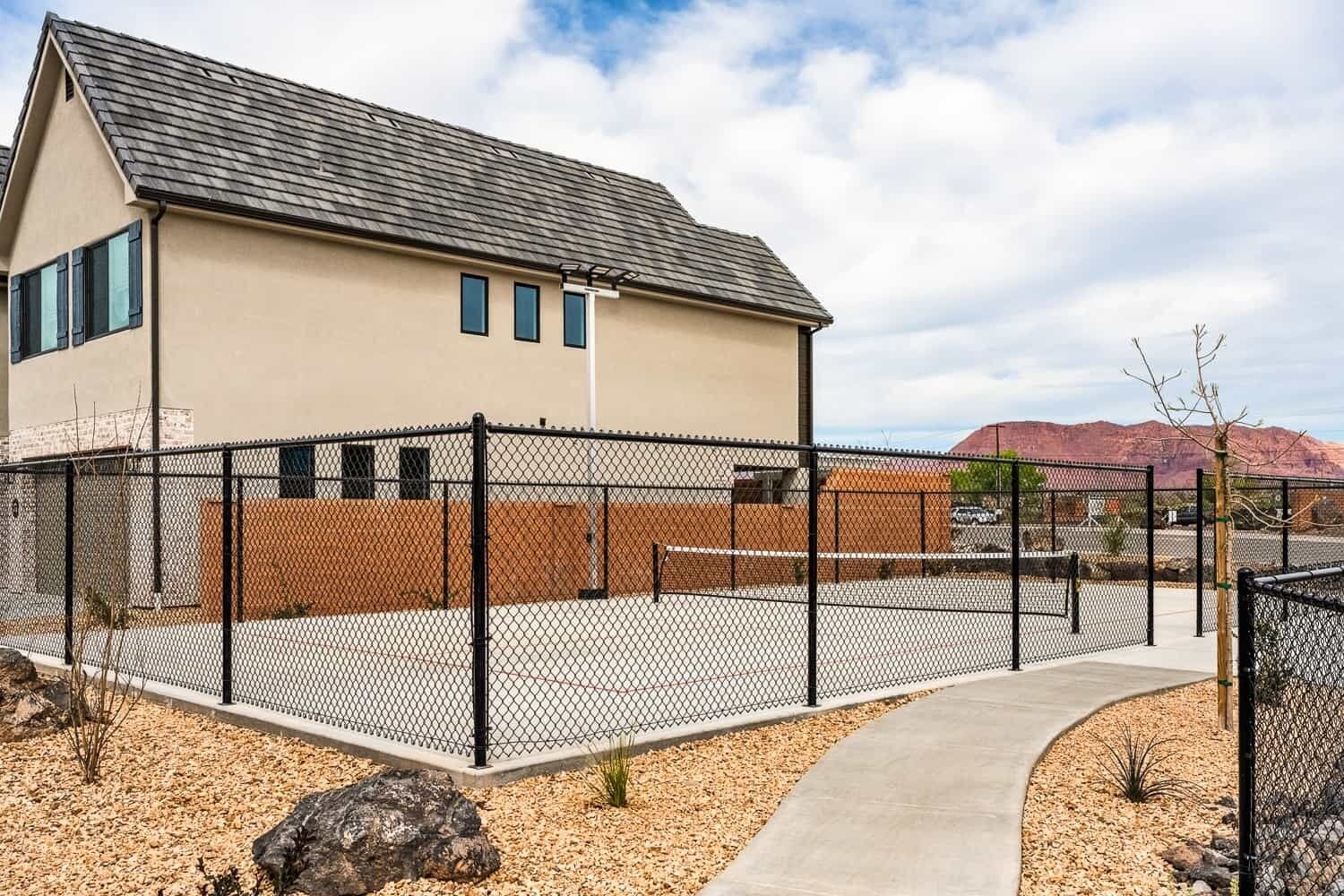 A modern building with a beige exterior, a black roof, and a chain-link fence surrounding a paved area.