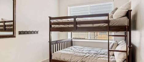 A bunk bed with a wooden frame, a window with blinds, and a mirror on the wall.