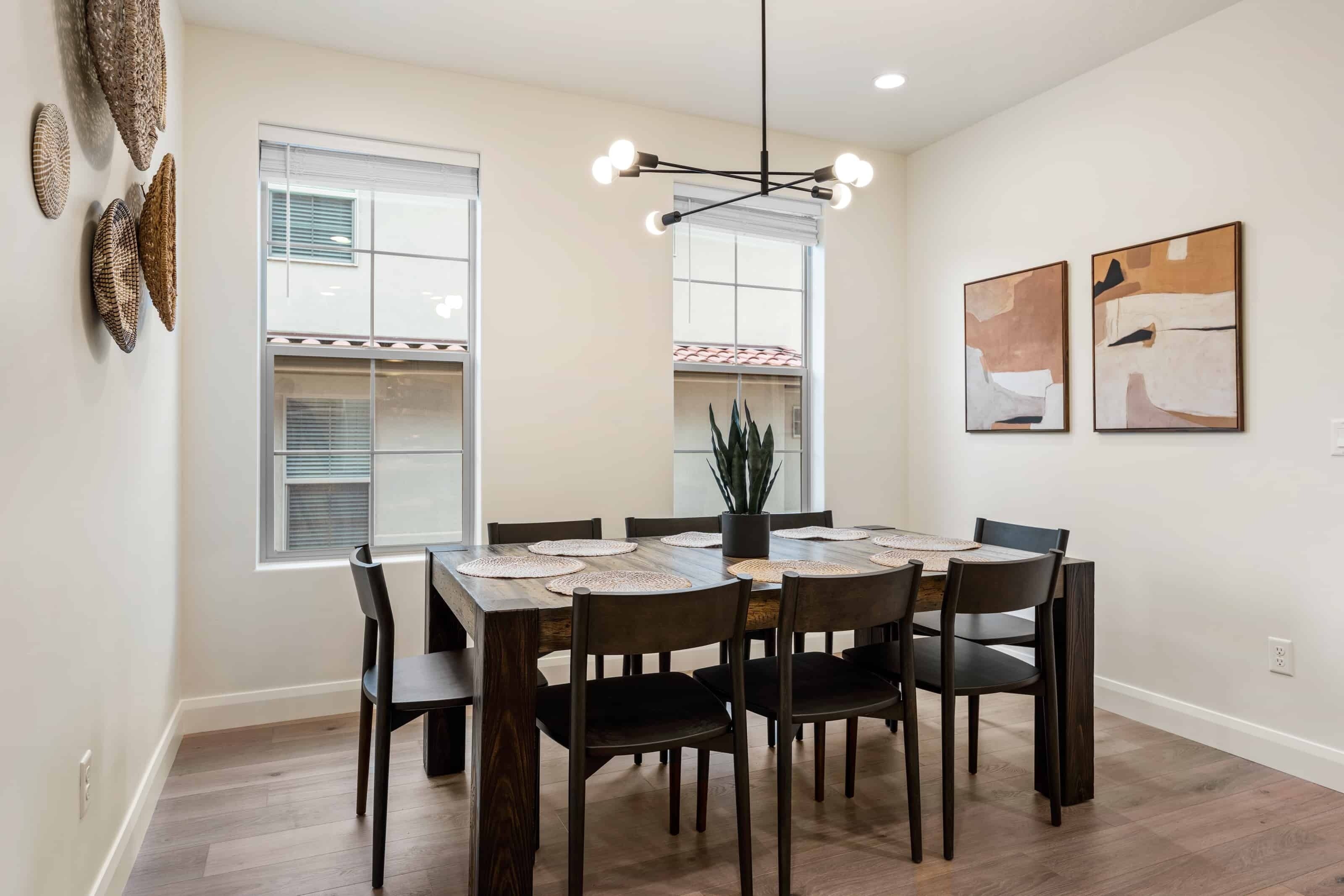 A dining area with a wooden table, six chairs, and a hanging light fixture.